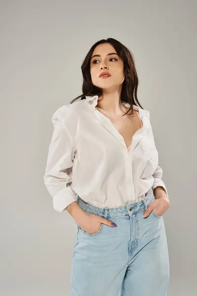 A beautiful, plus size woman posing gracefully in stylish white shirt and jeans against a gray backdrop. — Stock Photo