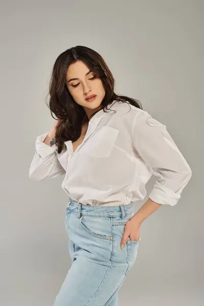 A stunning plus size woman poses in a trendy white shirt and jeans against a gray backdrop. — Stock Photo