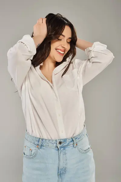 A beautiful plus size woman posing in stylish white shirt and jeans against a gray backdrop. — Stock Photo
