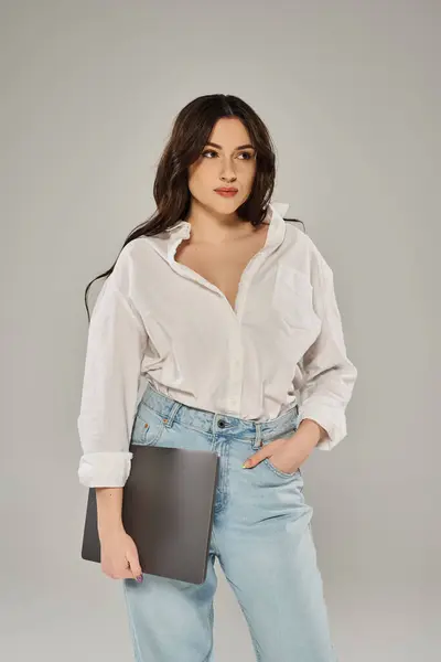 A beautiful plus-size woman in a white shirt and jeans holding a folder on a grey backdrop. — Photo de stock