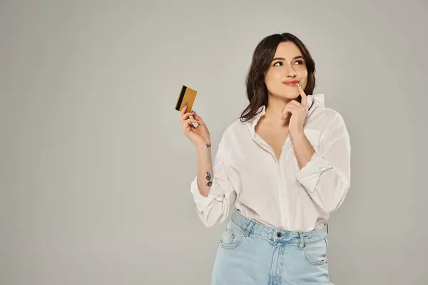 Plus size woman in white shirt exudes elegance while holding a gold card against a gray backdrop. — Stock Photo