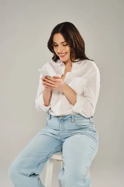 Eine modische Plus-Size-Frau, stilvoll gekleidet, sitzt auf einem Schemel, während sie ein Handy benutzt. — Stockfoto