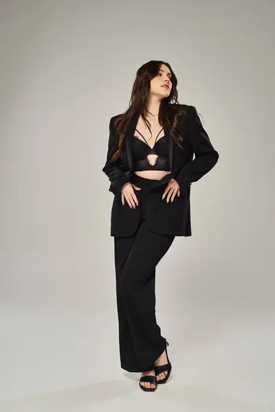A stunning plus-size woman in a sleek black suit confidently poses against a gray backdrop. — Stock Photo