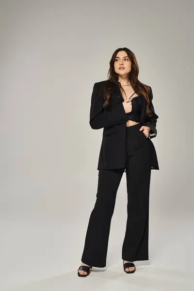 A beautiful plus size woman exuding confidence and style while posing in a black suit against a gray backdrop. — Stock Photo
