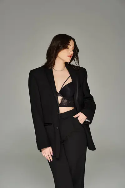 Uma mulher deslumbrante plus-size em um terno preto elegante marcando uma pose confiante contra um pano de fundo cinza. — Fotografia de Stock