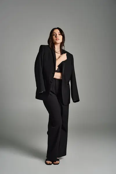 A stunning plus-size woman showcases her elegance in a chic black suit against a sleek gray backdrop. — Stock Photo