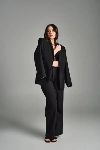 A beautiful plus size woman exudes elegance in a black suit, striking a confident pose against a gray backdrop. — Stock Photo