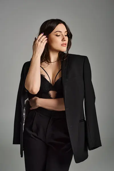 Uma bela mulher plus size vestida com um terno preto atinge uma postura confiante contra um pano de fundo cinza. — Fotografia de Stock