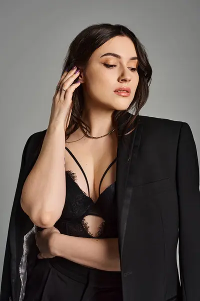 A beautiful plus-size woman exudes confidence in a black suit and bra against a gray backdrop. — Stock Photo