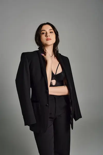 Uma bela mulher plus-size posa confiantemente em um terno preto elegante contra um pano de fundo cinza. — Fotografia de Stock