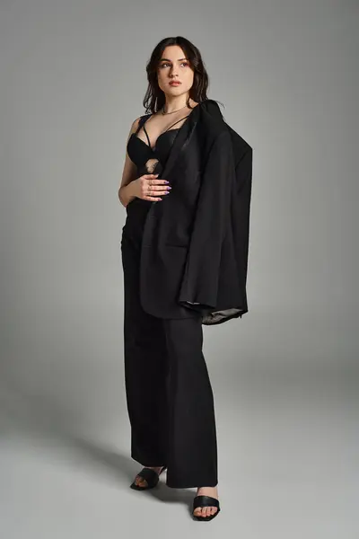 Mujer de talla grande exudando elegancia en un vestido negro y chal contra un fondo gris. - foto de stock