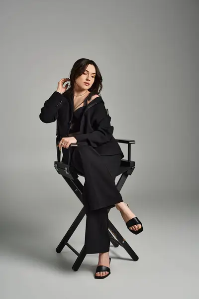 A beautiful plus size woman poses stylishly in a chair against a gray backdrop. — Stock Photo