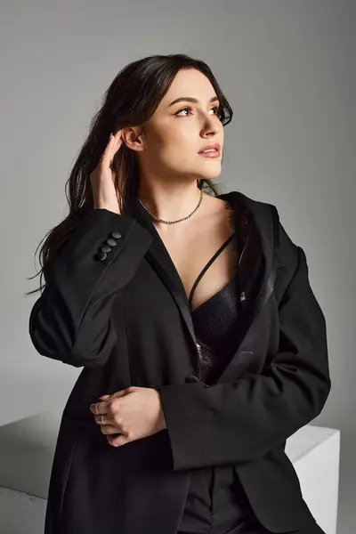 Eine schöne Plus-Size-Frau posiert in einem eleganten schwarzen Anzug vor grauem Hintergrund und strahlt Selbstbewusstsein und Stil aus. — Stockfoto
