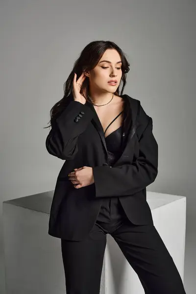 Plus size woman exuding confidence in a sleek black suit striking a pose on a gray backdrop. — Stock Photo