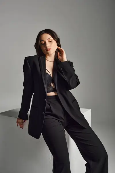 A stunning plus size woman in a black suit strikes a confident pose against a neutral gray backdrop. — Stock Photo