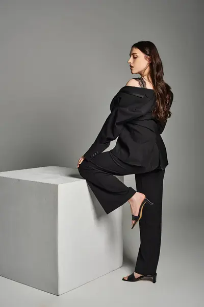 Uma bela mulher plus size está posando confiantemente em top preto e calças contra um pano de fundo cinza. — Fotografia de Stock