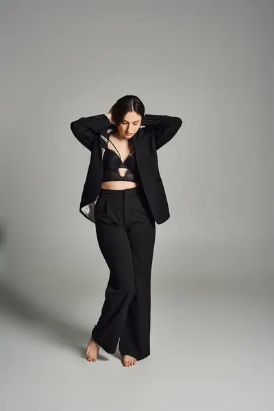 Uma bela mulher plus size transpira confiança em um terno preto impressionante, marcando uma pose contra um pano de fundo cinza. — Fotografia de Stock