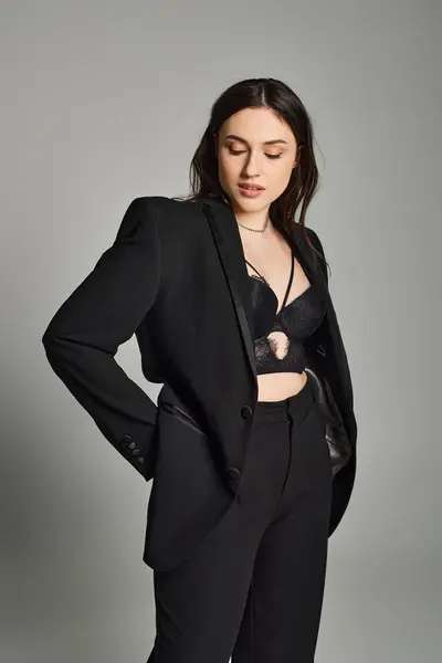 Eine atemberaubende Plus-Size-Frau in einem eleganten schwarzen Anzug posiert selbstbewusst vor grauem Hintergrund. — Stockfoto