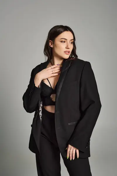 A beautiful plus size woman in a black suit striking a confident pose against a gray backdrop. — Stock Photo