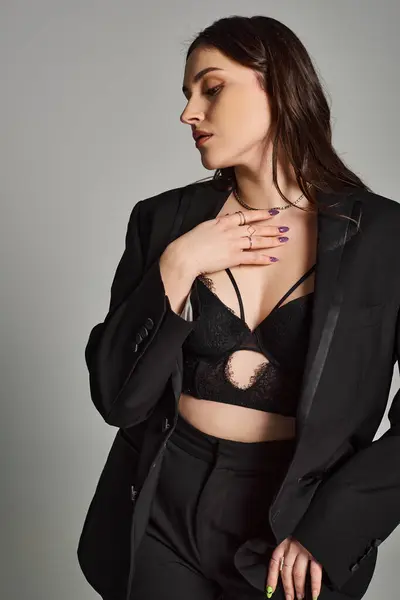 A stunning plus size woman confidently poses in a black suit and bra against a gray backdrop. — Photo de stock