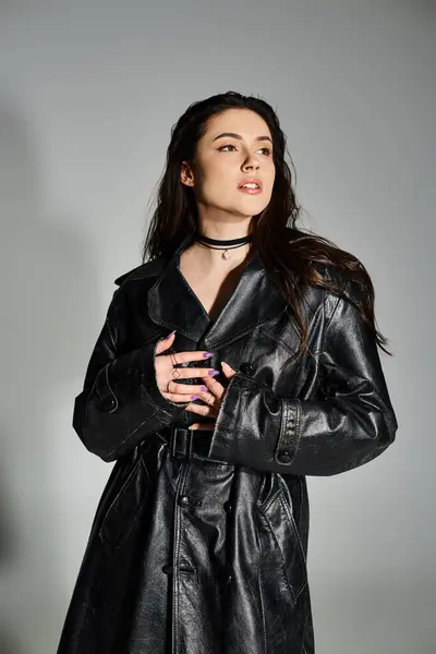 A beautiful plus size woman exudes confidence and style in a black leather coat while posing on a gray backdrop. — Stock Photo