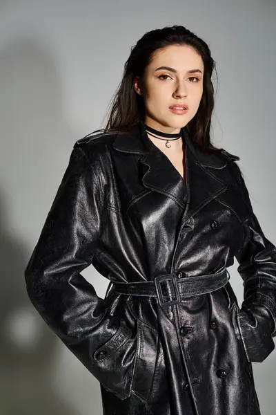 Eine atemberaubende Plus-Size-Frau strahlt in einem schwarzen Leder-Trenchcoat vor neutralem grauen Hintergrund Zuversicht aus. — Stockfoto
