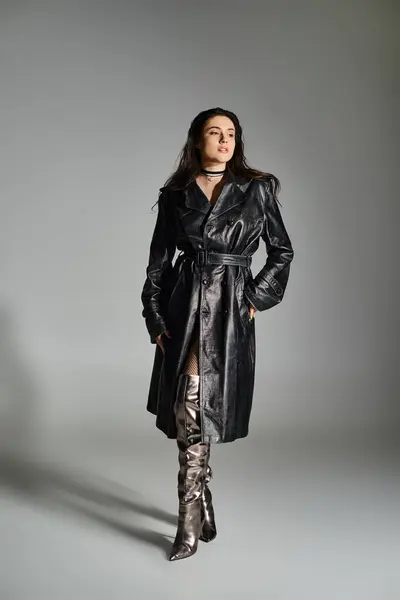 Eine atemberaubende Plus-Size-Frau posiert in stylischem schwarzen Mantel und Stiefeln vor grauem Hintergrund. — Stockfoto