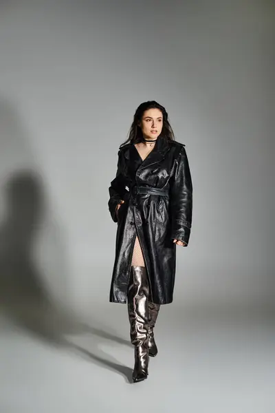 Eine atemberaubende Plus-Size-Frau posiert in einem eleganten schwarzen Mantel und Stiefeln vor neutralem Hintergrund. — Stockfoto