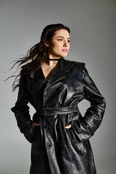 Eine schöne Plus-Size-Frau posiert anmutig in einem schicken schwarzen Leder-Trenchcoat vor neutralem grauen Hintergrund. — Stockfoto