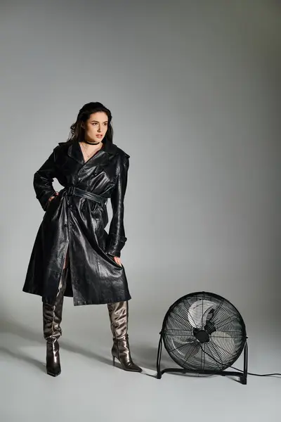 Impressionante mais tamanho senhora em casaco preto chique e botas de pé graciosamente ao lado de um ventilador retro em fundo cinza. — Fotografia de Stock