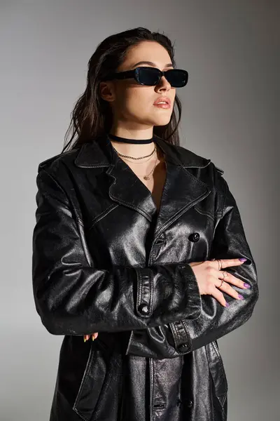 Una hermosa mujer de talla grande posando en una chaqueta de cuero negro y gafas de sol sobre un fondo gris. - foto de stock