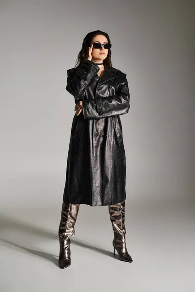 A plus size woman exudes confidence in a stylish black leather coat and boots against a gray backdrop. — Photo de stock
