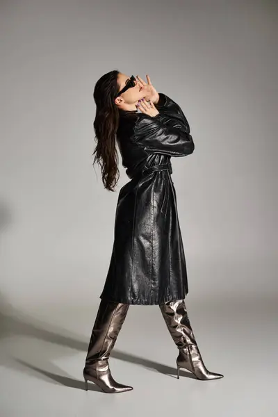 Curvy woman exudes confidence in a black leather coat and boots against a gray backdrop. — Stock Photo