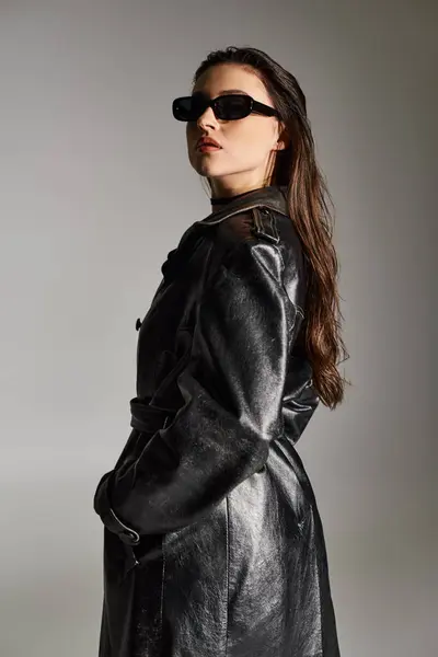 Eine Plus-Size-Frau strahlt Stil in schwarzem Mantel und Sonnenbrille vor grauem Hintergrund aus und tritt selbstbewusst in Pose. — Stockfoto