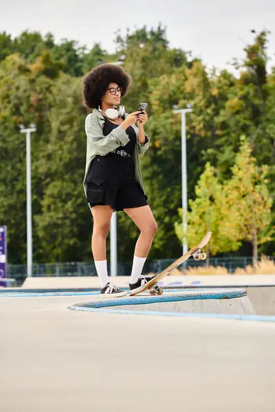 Junge Afroamerikanerin mit lockigem Haar steht selbstbewusst auf einem Skateboard in einem lebhaften Skatepark. — Stockfoto
