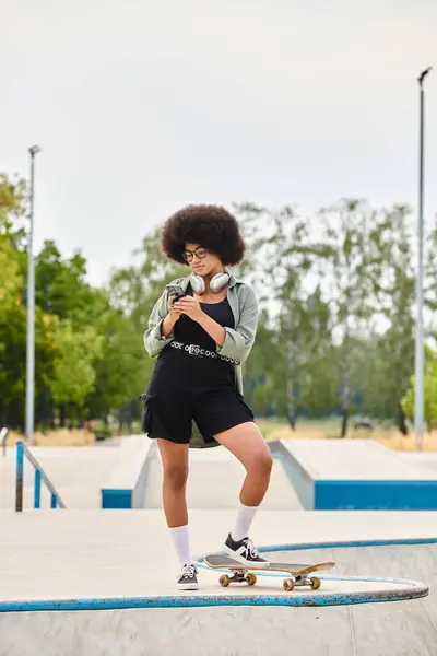 Ein afroamerikanischer Teenager mit lockigem Haar steht selbstbewusst mit einem Skateboard in einem Skatepark. — Stockfoto