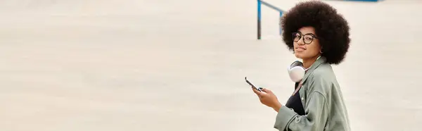 Una donna elegante con una pettinatura afro utilizzando un telefono cellulare. La scena urbana cattura la sua essenza mentre si connette con la tecnologia. — Foto stock