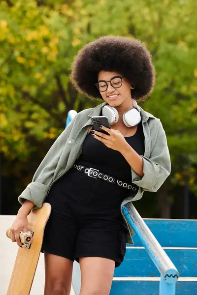 Energetische Afroamerikanerin mit lockigem Haar, Kopfhörern und Skateboard in einem Skatepark. — Stockfoto