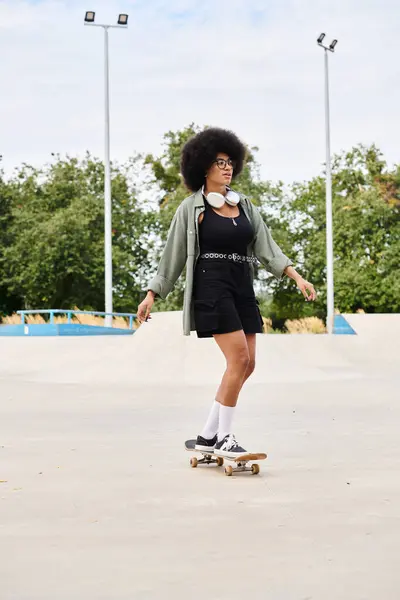 Eine qualifizierte junge Afroamerikanerin mit lockigem Haar skateboards anmutig auf einem Zementfeld in einem Skatepark. — Stockfoto