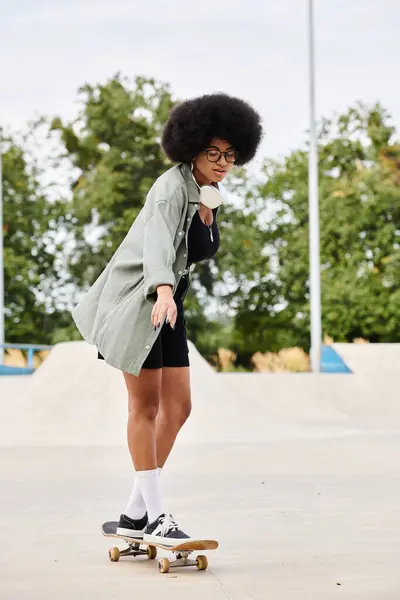 Una joven afroamericana con el pelo rizado patinando sobre una superficie de cemento en un parque de skate. - foto de stock