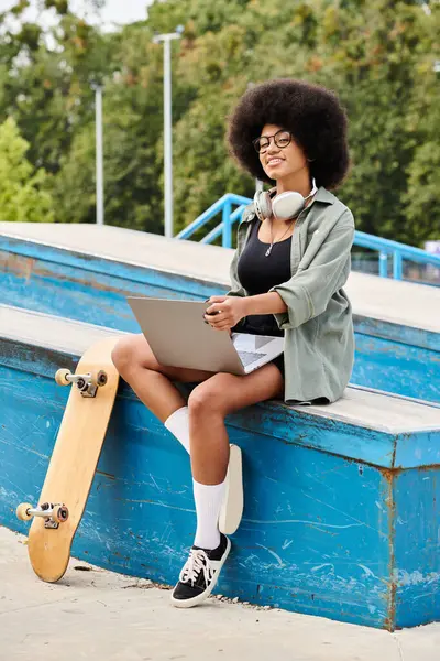 A young African American woman with curly hair sitting on a bench with her skateboard at an outdoor skate park. — Stock Photo