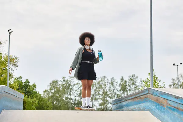 Una mujer elegante con un peinado afro sostiene una botella de agua. - foto de stock