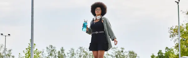 Joven mujer afroamericana con un pelo rizado afro montando un monopatín en un parque de skate. - foto de stock