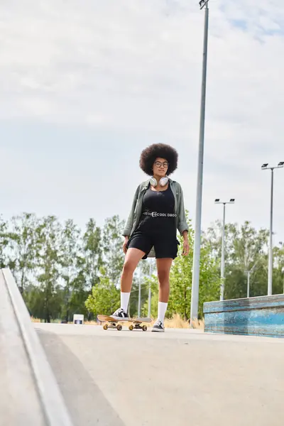 Una giovane donna afroamericana con i capelli ricci con sicurezza skateboard lungo un marciapiede della città in una giornata di sole. — Foto stock