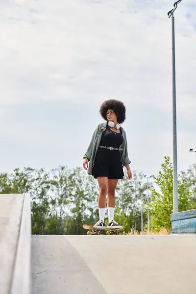Une jeune femme afro-américaine aux cheveux bouclés descend une rampe dans un skate park. — Photo de stock