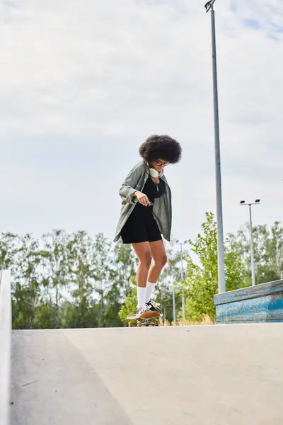 Uma jovem afro-americana com cabelo encaracolado monta confiantemente um skate até uma rampa de cimento em um parque de skate ao ar livre. — Fotografia de Stock