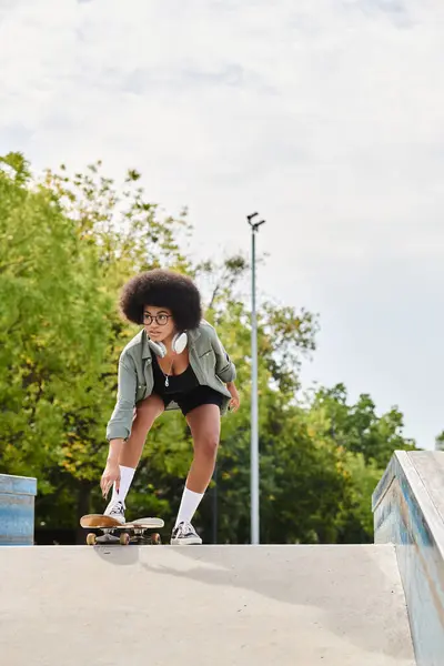 Молодая афроамериканка с кудрявыми волосами на скейтборде по склону пандуса в ярком открытом скейт-парке. — стоковое фото