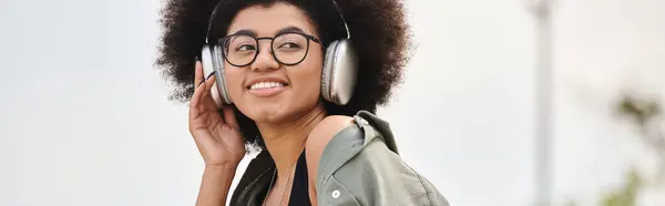 A young woman in a jacket listens to music through headphones while embodying the rhythm in an urban setting. — Stock Photo