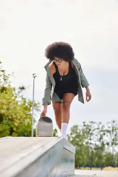 A young African American woman with curly hair glides on a skateboard in a skate park. — Stock Photo