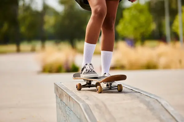 Una joven afroamericana realiza un atrevido truco de skate en una cornisa en un parque urbano de skate. - foto de stock